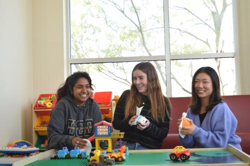 Three undergraduate research assistants are smiling and laughing while cleaning children's toys in a play room