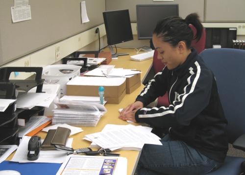An undergraduate research assistant sitting at a desk, and stuffing envelopes with the lab newsletter