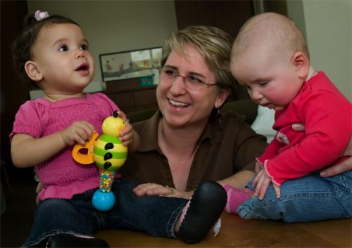Lisa playing with two babies. Lisa is in the middle with a baby on her left and on her right