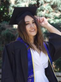 A picture of Gabi wearing a black graduation cap and gown over a white dress..