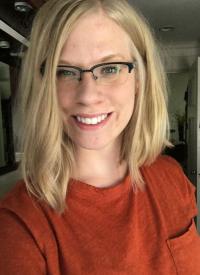 A selfie of Michaela. She is wearing glasses and a redish orange shirt.